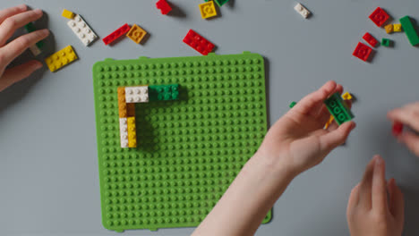 Overhead-Shot-Of-Two-Children-Playing-With-Plastic-Construction-Bricks-On-Grey-Background-1